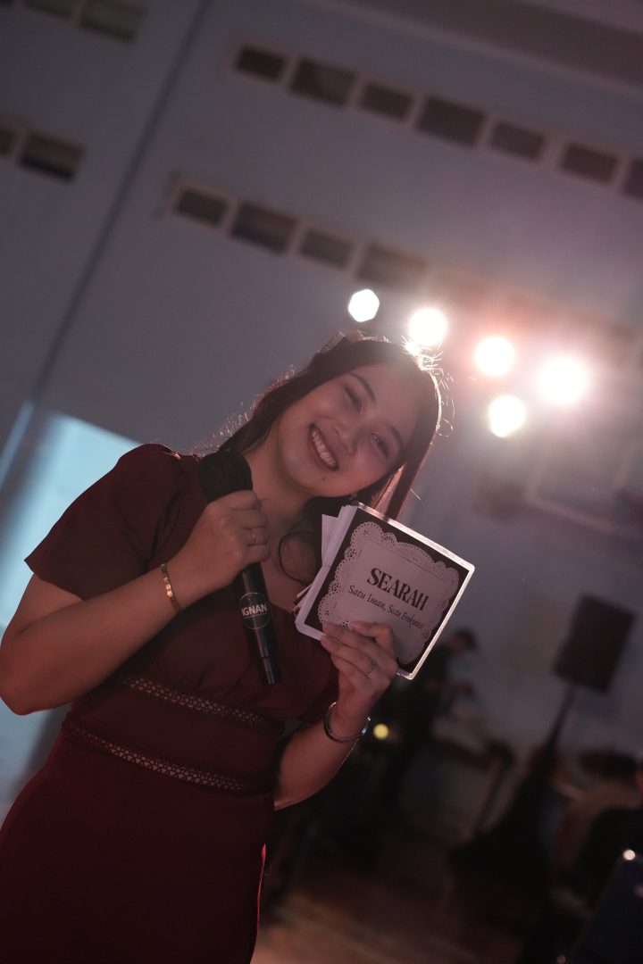 Pembawa acara memegang wireless microphone IGNAN Audio dan kartu susunan acara SEARAH